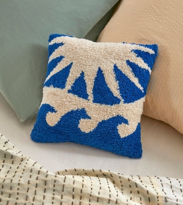 blue and white tufted pillow with a minimalist wave and a sun print