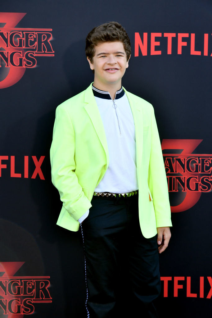 Gaten with short hair, bright blazer, and pants