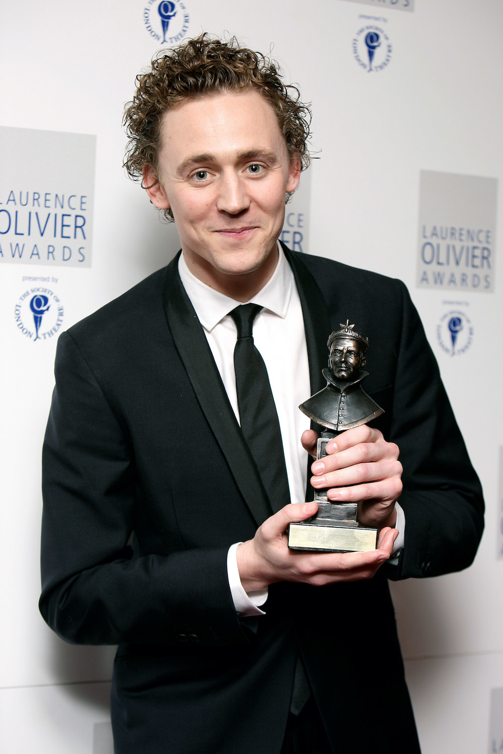 close up of Hiddleston holding an award with long curly hair