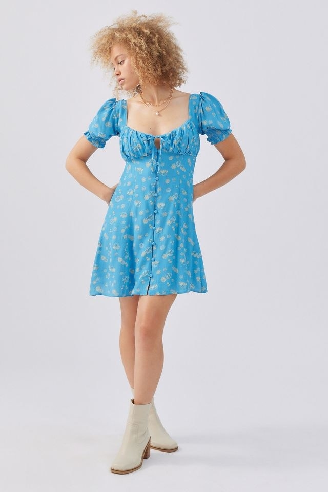 model in bright blue floral patterned mini dress with buttons up the front, a ruched chest and keyhole cutout