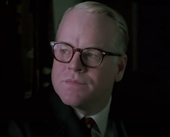 Philip Seymour Hoffman as Truman Capote speaking to someone while gazing out of a window