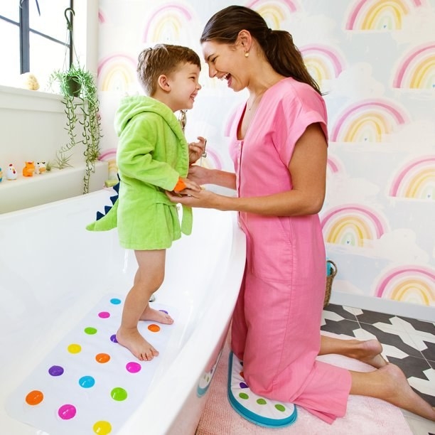 Model kneeling on bath mat holding kids hands
