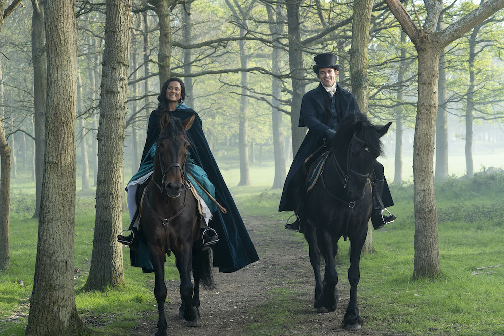 Simone and Jonathan rising horses amid trees in a scene from Bridgerton