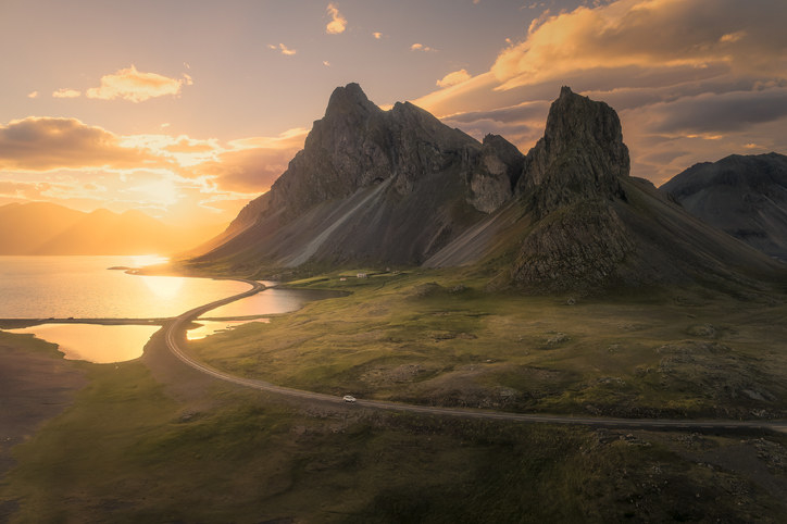 A view of a sunset over mountains, a body of water, and a road with a car on it