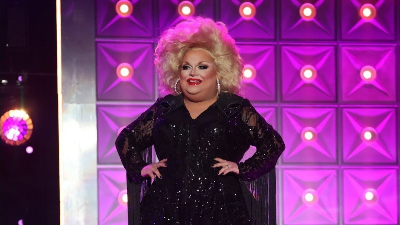 A drag queen stands onstage with their hands on their hips