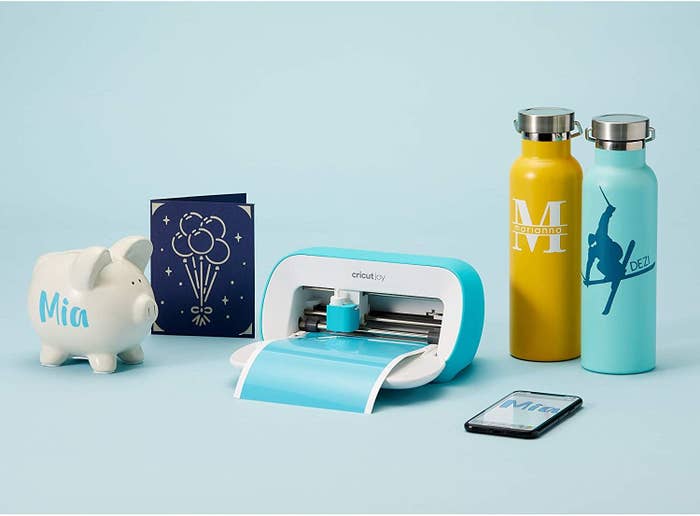 A Cricut Joy machine with water bottles, a card, and a phone next to it
