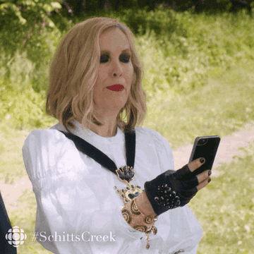 A gif of Moira from Schitt&#x27;s Creek looking at her phone surprised