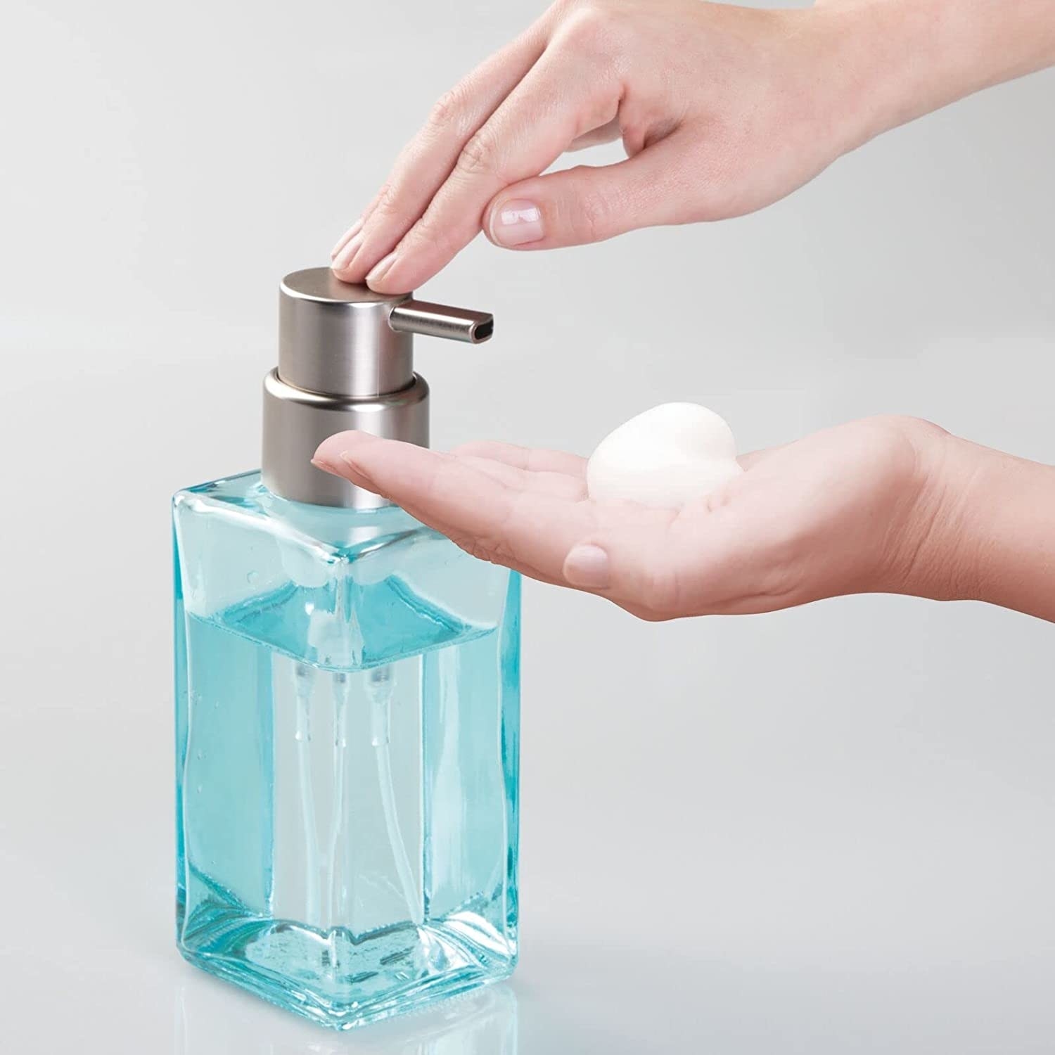 Model using the light blue soap dispenser with clear blue soap to dispense some foam onto their hand