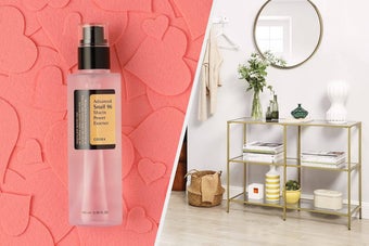 A bottle of essence on a pile of felt hearts, A gold console table against a wall with magazines and vases on the shelves