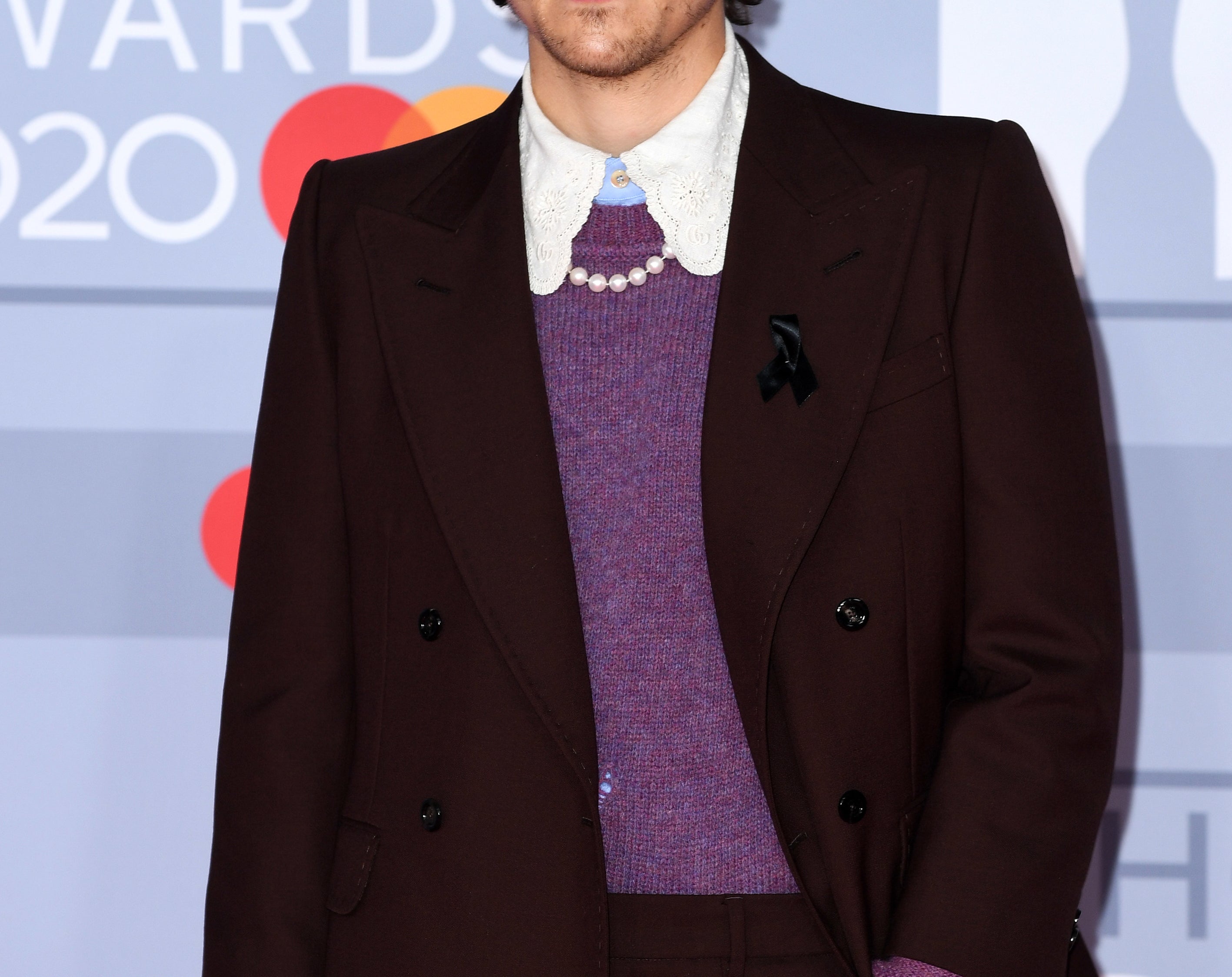 A close-up of Harry in a jacket and lacy collar top underneath a sweater