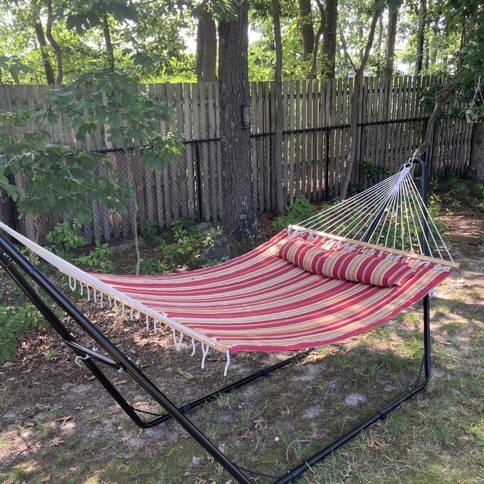 a reviewer photo of the red striped hammock and stand in a backyard