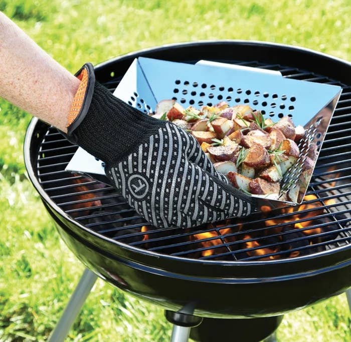 Model wearing achromatic and grey grill mitt holding cookware of potatoes implicit achromatic grill