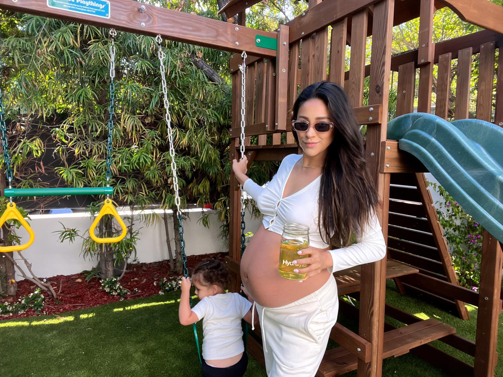 a pregnant Shay plays outside with Atlas in their backyard playground
