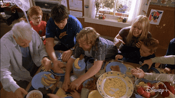 Kids and adults around a kitchen table scrambling for food in a scene from Cheaper by the Dozen