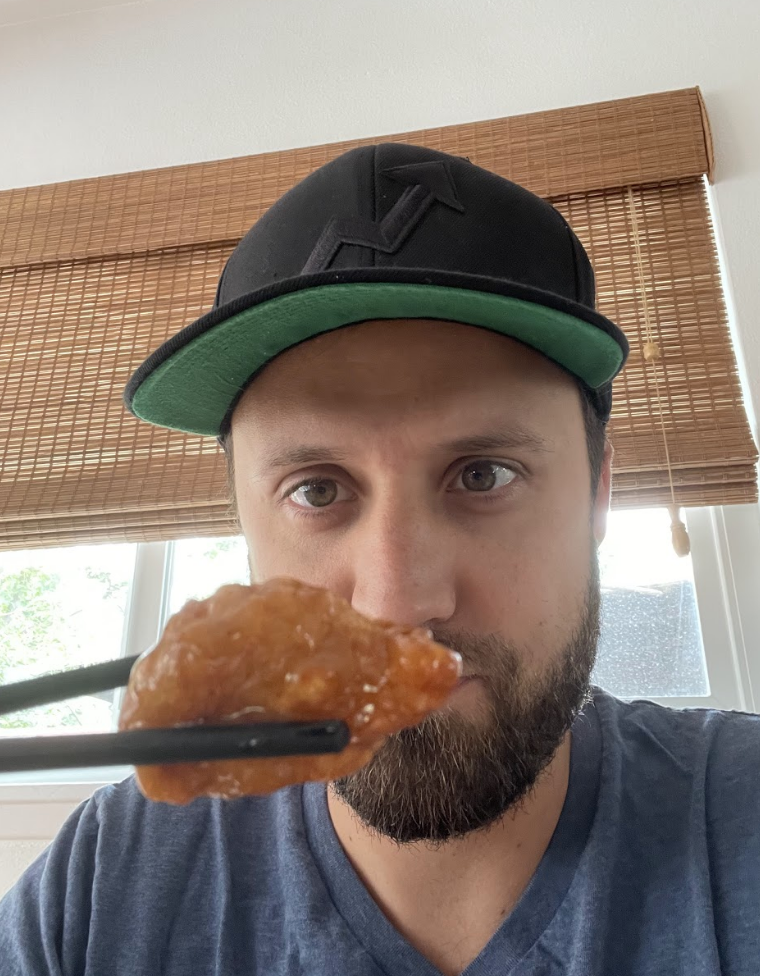 Andy Golder holding a piece of orange chicken in front of his face