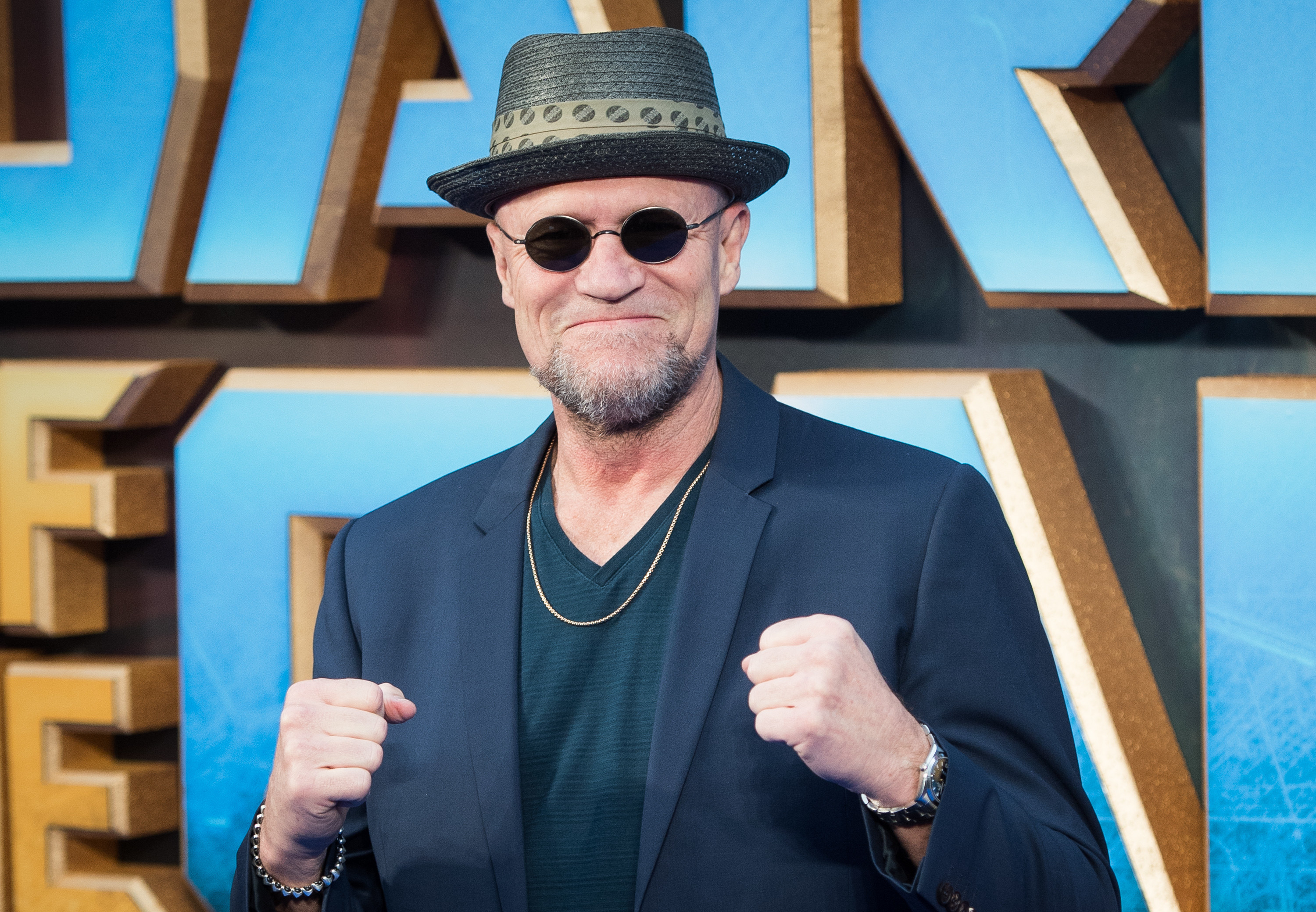 Michael at the Guardians of the Galaxy premiere, wearing a navy blazer with a similar colour V-neck t-shirt beneath, with a straw fedora with a ribbon around it.