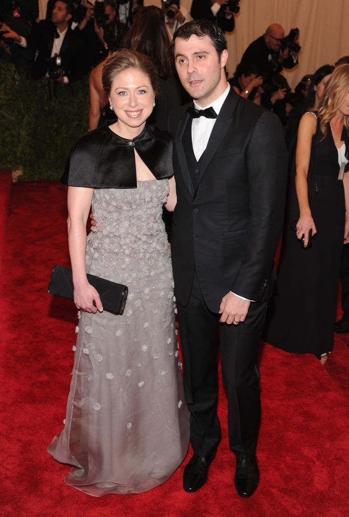 Chelsea wearing a gray dress with small flowers pinned to it, and Marc wearing a black suit