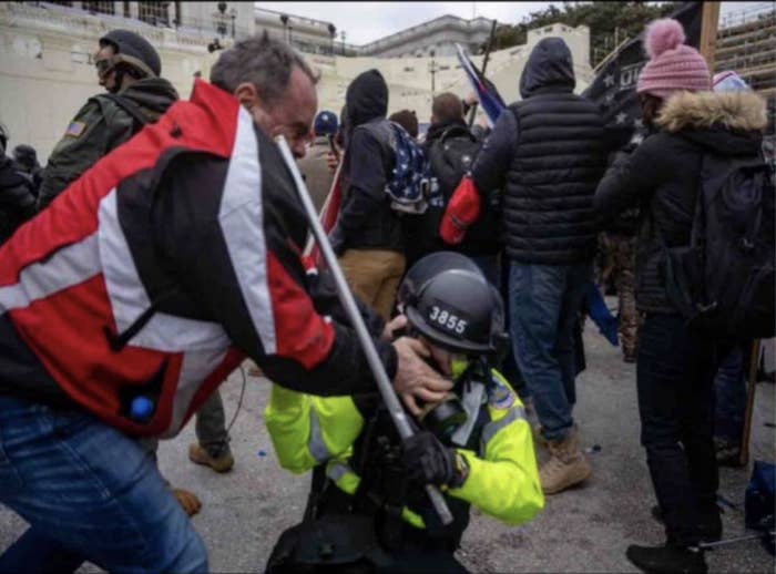 A standing man grabs at the face of a police officer on the ground