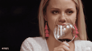 A woman rolling her eyes and shaking her head as she takes a sip of wine.