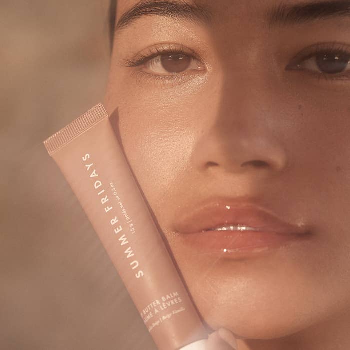 a person holding up a tube of the balm next to their glossy lips