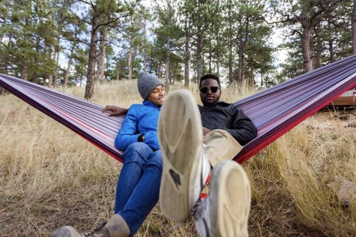 Two people relaxing in the red and purple hammock hung from trees
