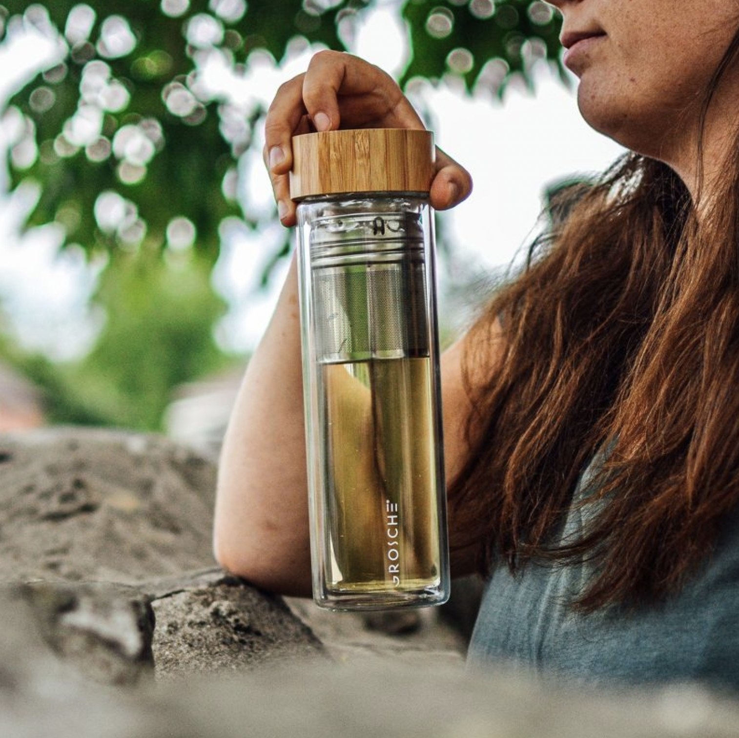 Model holding the clear glass water bottle filled with infused tea with wooden lid screwed on