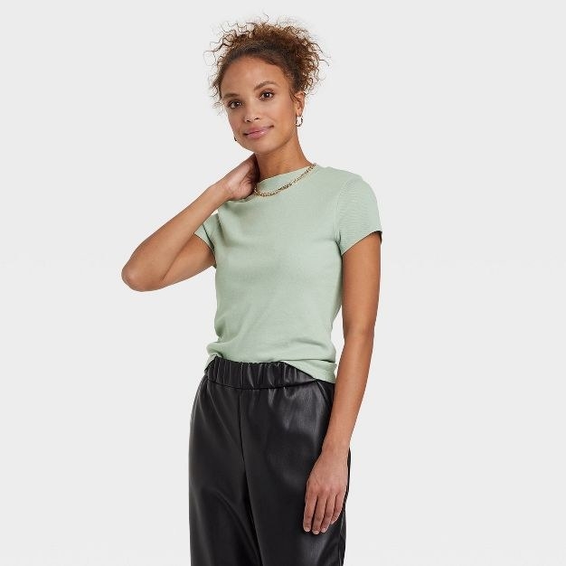 The model wears the light green top with shiny black pants