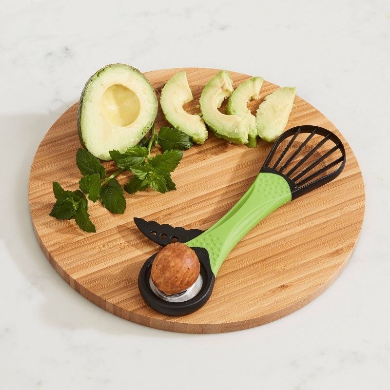 The tool with pit removed from avocado and half of it sliced evenly