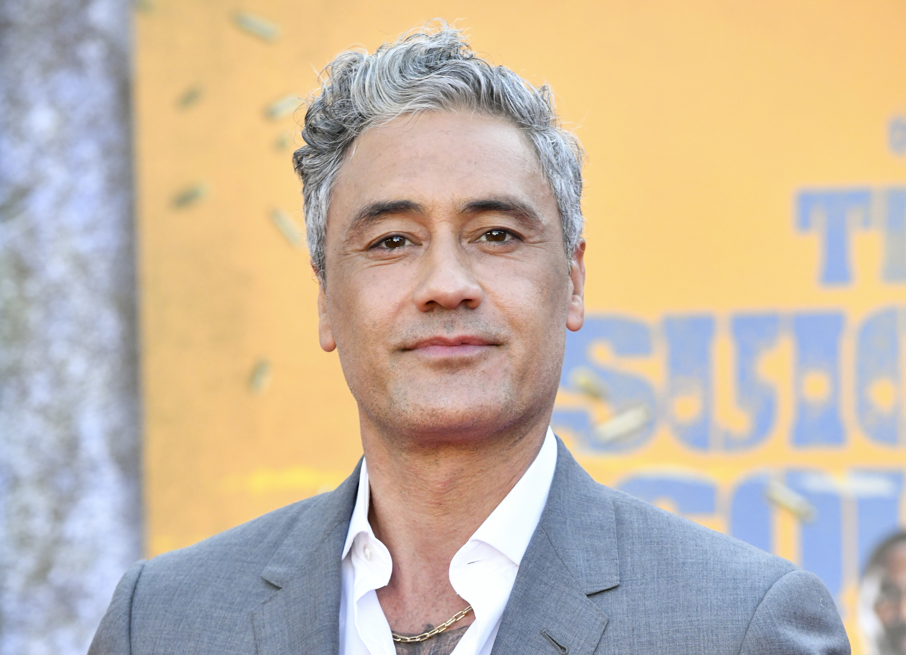 Taika smiling in a grey suit jacket with an open necked white shirt