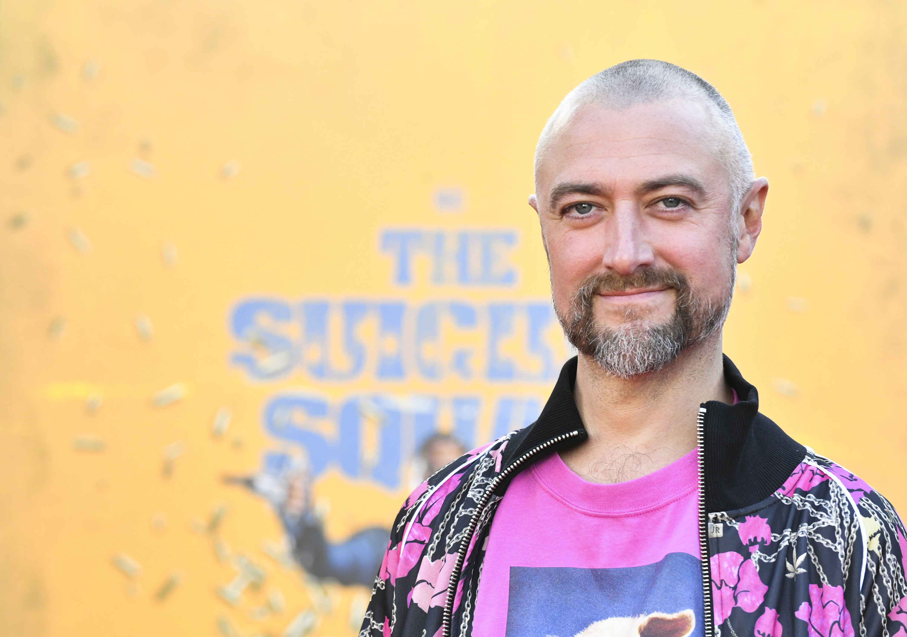 Sean smiling, wearing a bright pink t-shirt with a black jacket with bright pink details over the top