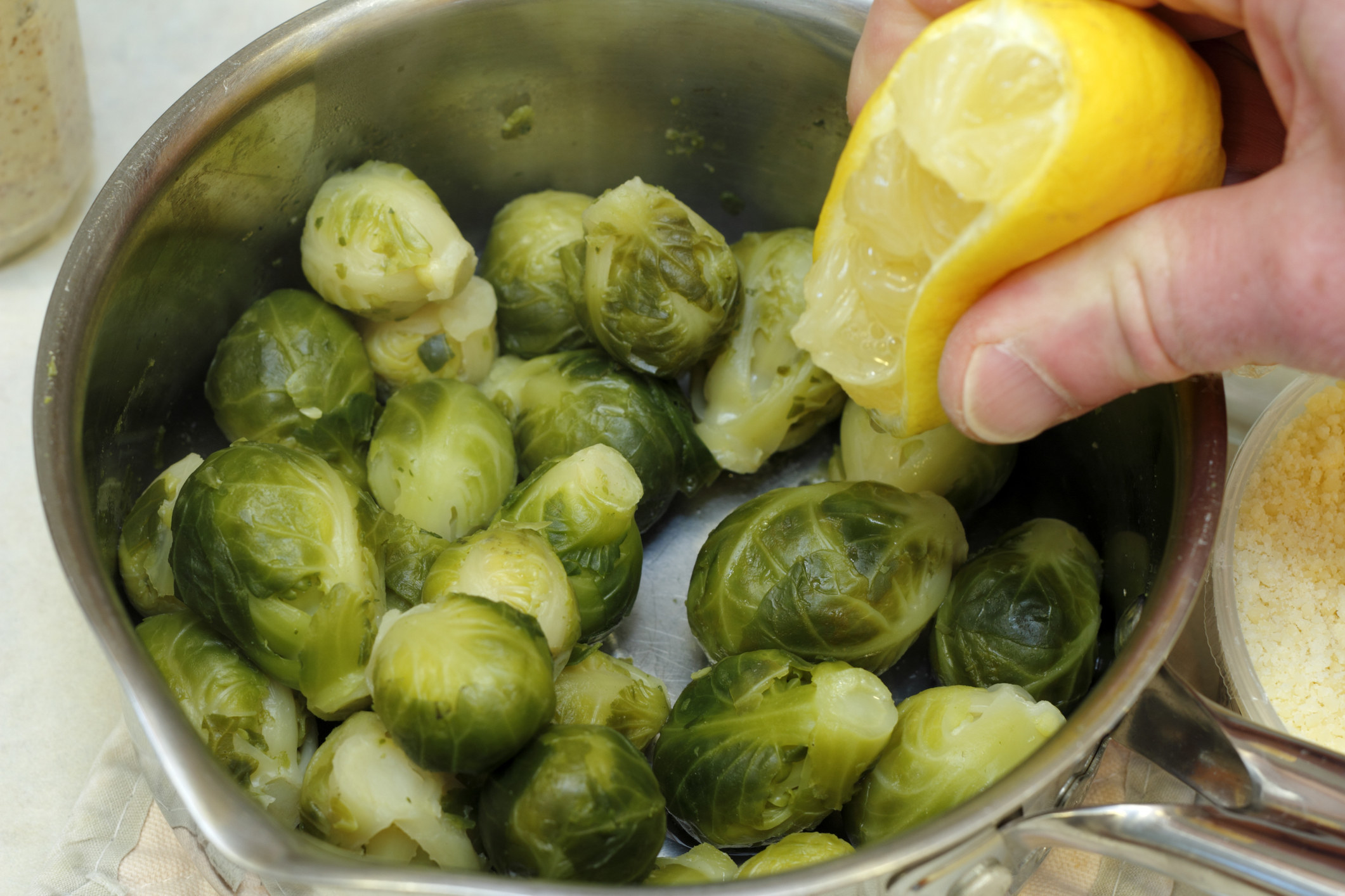 Hand-squeezing lemon juice from a fresh lemon onto cooked Brussels sprouts