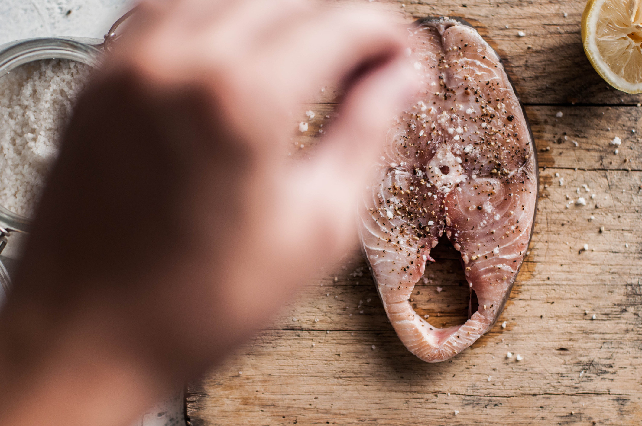 An above-view of a person seasoning a fish steak