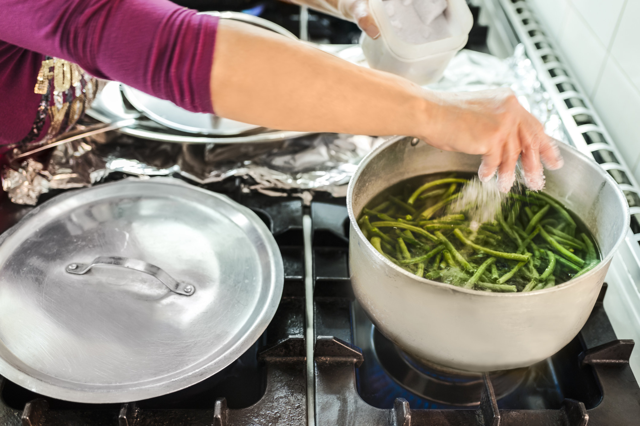 A woman boiling green beans with salt