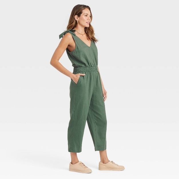 The model wears the green jumpsuit with neutral-colored shoes