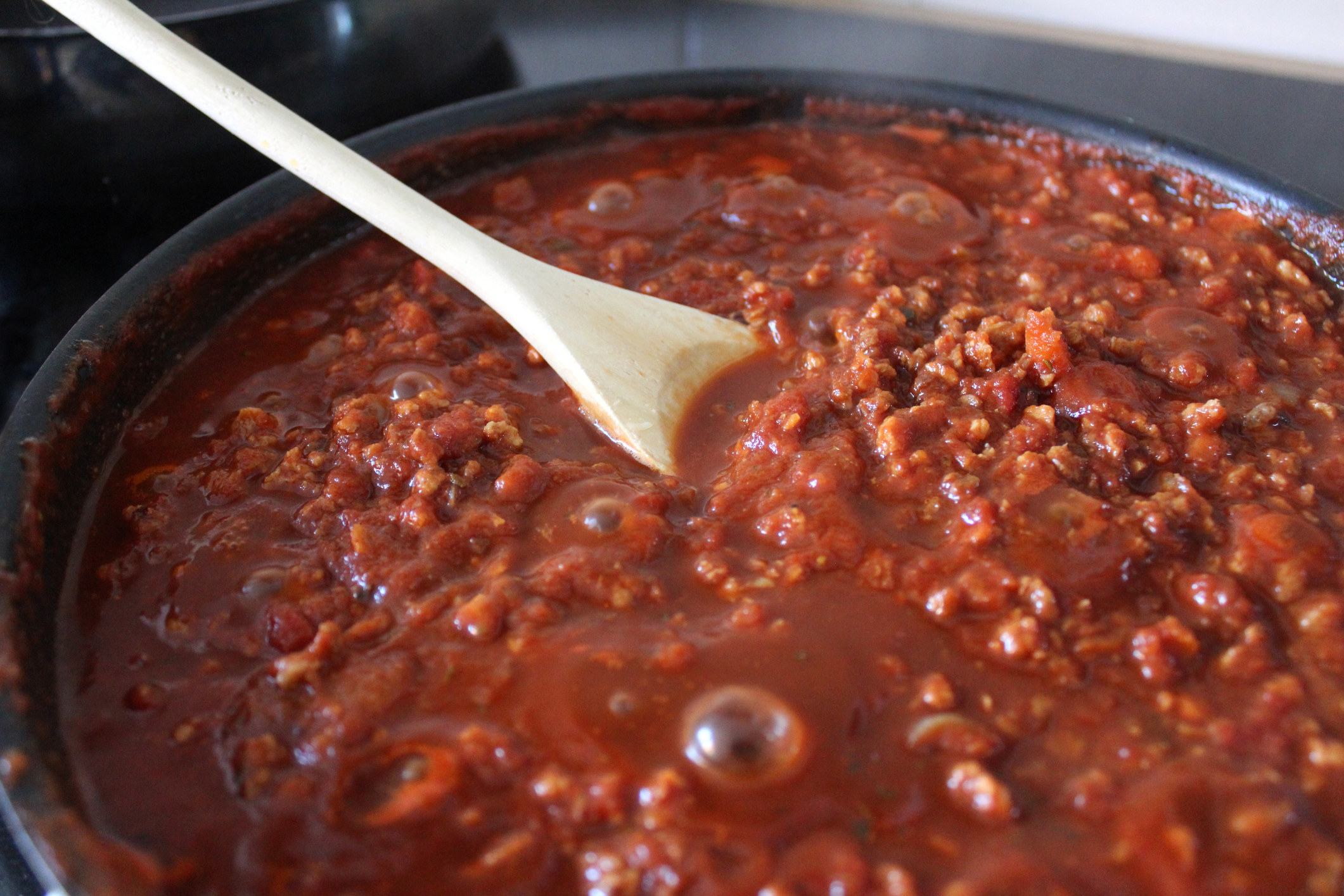 A wooden spoon stirring Bolognese sauce