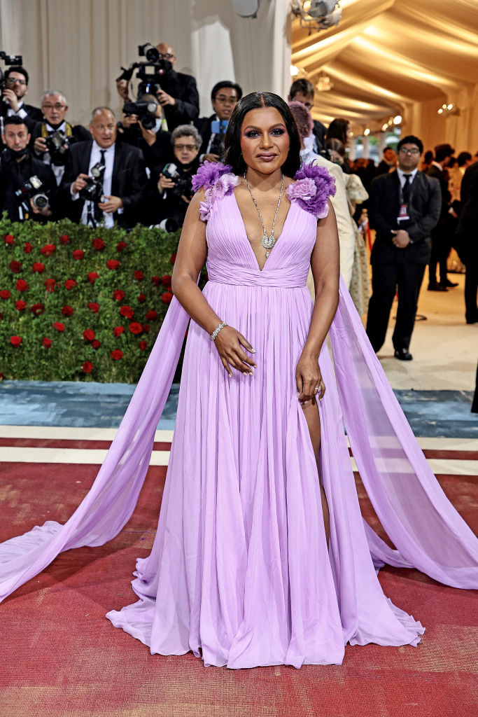 Mindy Kaling in a flowy gown with a slit, trains on either side, and flower embellishments