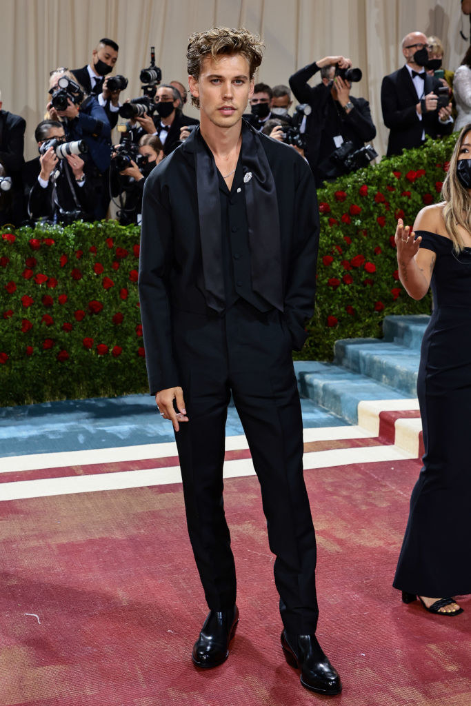 Austin Butler wearing a slim-fitting dark suit and shiny shoes