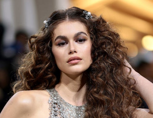 Kaia Gerber with dramatic eyebrows and big, curly hair fastened at the top with barrettes