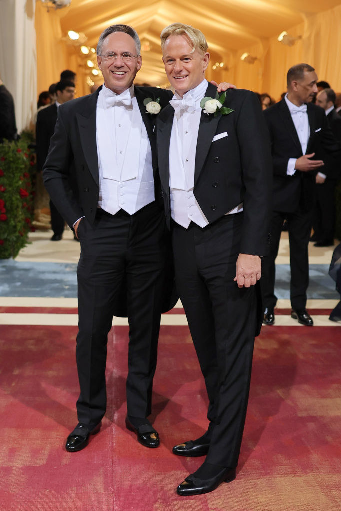 Andrew Saffir and Daniel Benedict wear matching tuxes and stand together and smile on the red carpet