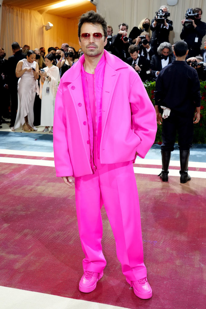 Sebastian Stan in a bright pink overcoat, suit, and sneakers