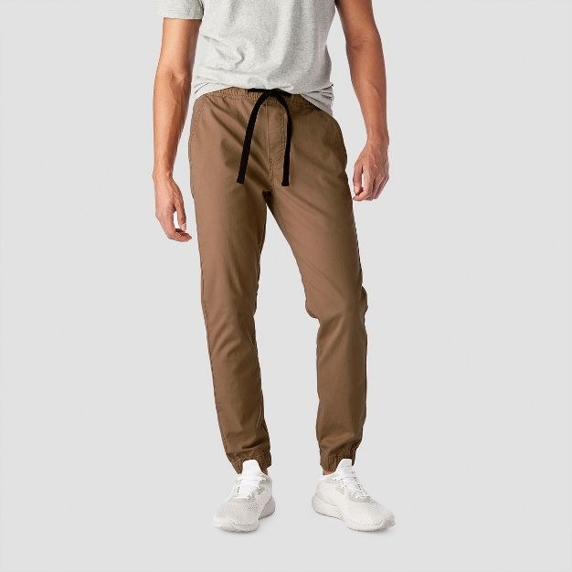 The model wears the brown joggers with white shoes and a heather grey T-shirt
