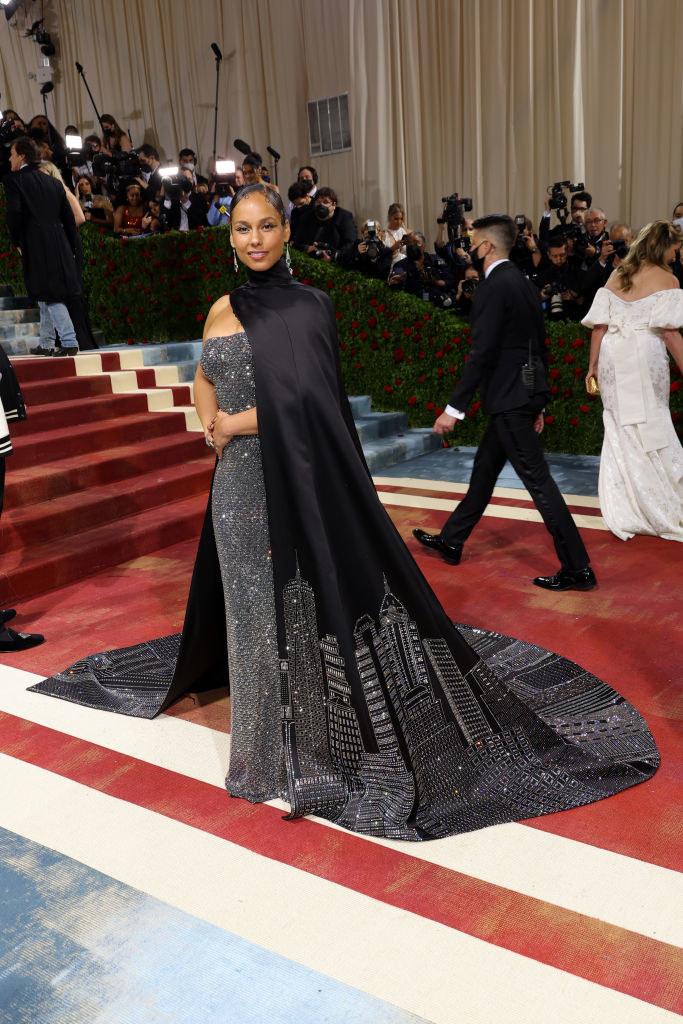 Alicia Keys smiles and wears a dress that has a city skyline on its train