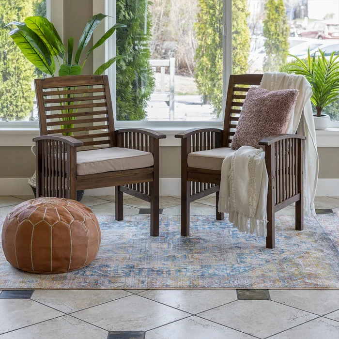 A pair of wooden chairs on a small rug with a leather pouf next to them
