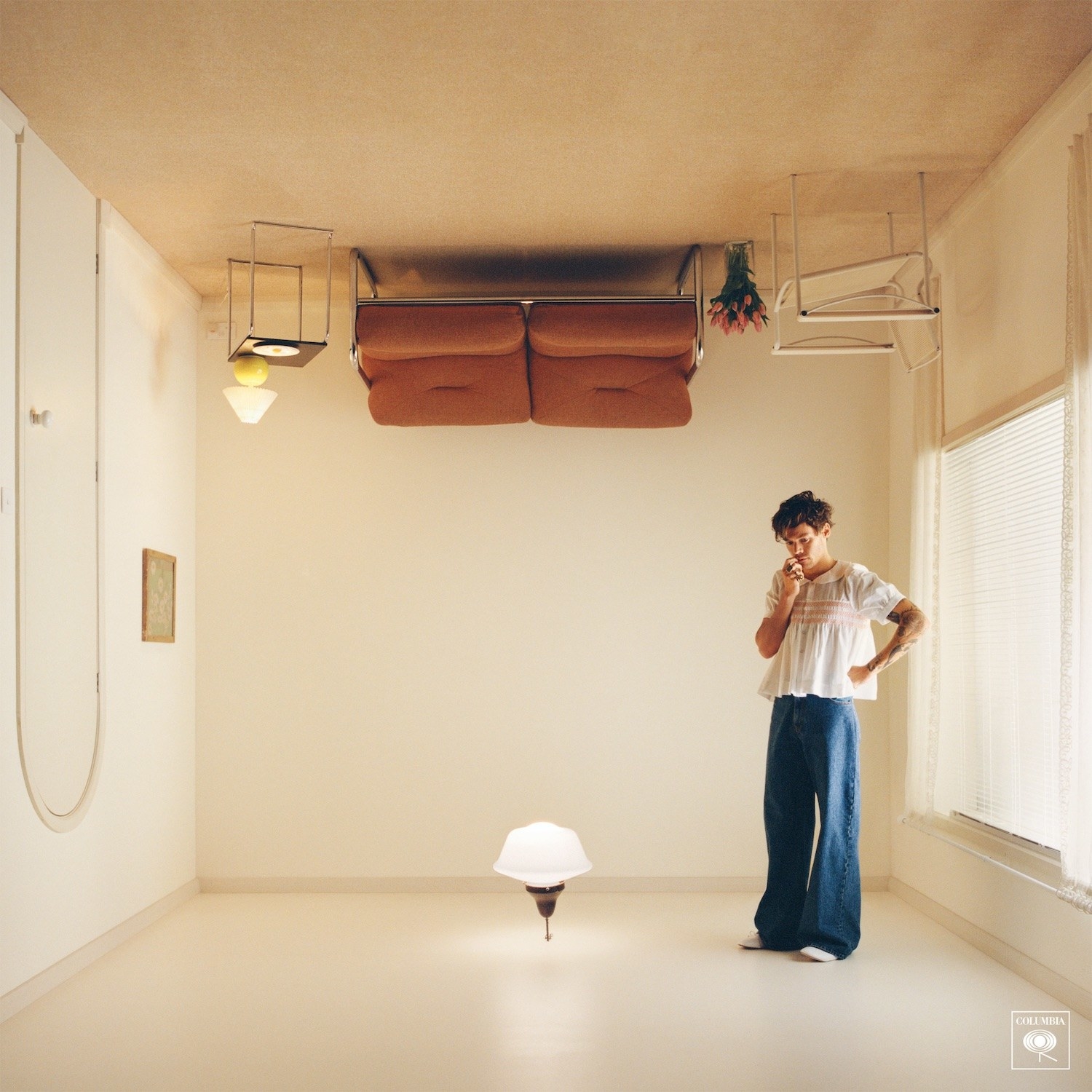 Styles stands on the ceiling in a simple living room flipped upside down