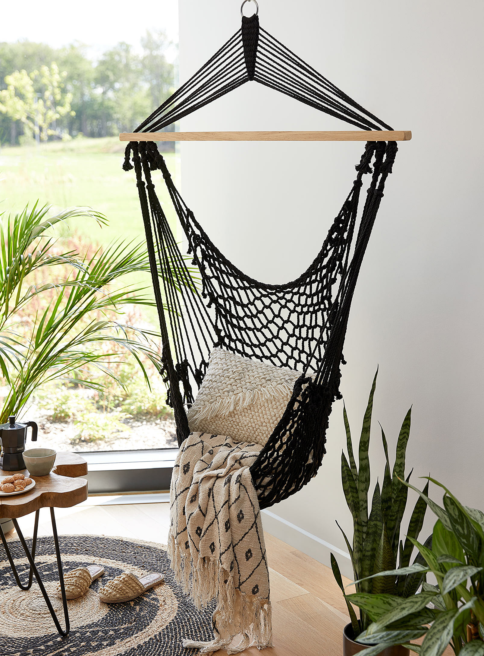 A crochet hammock hanging from a ceiling with a blanket and throw pillow resting