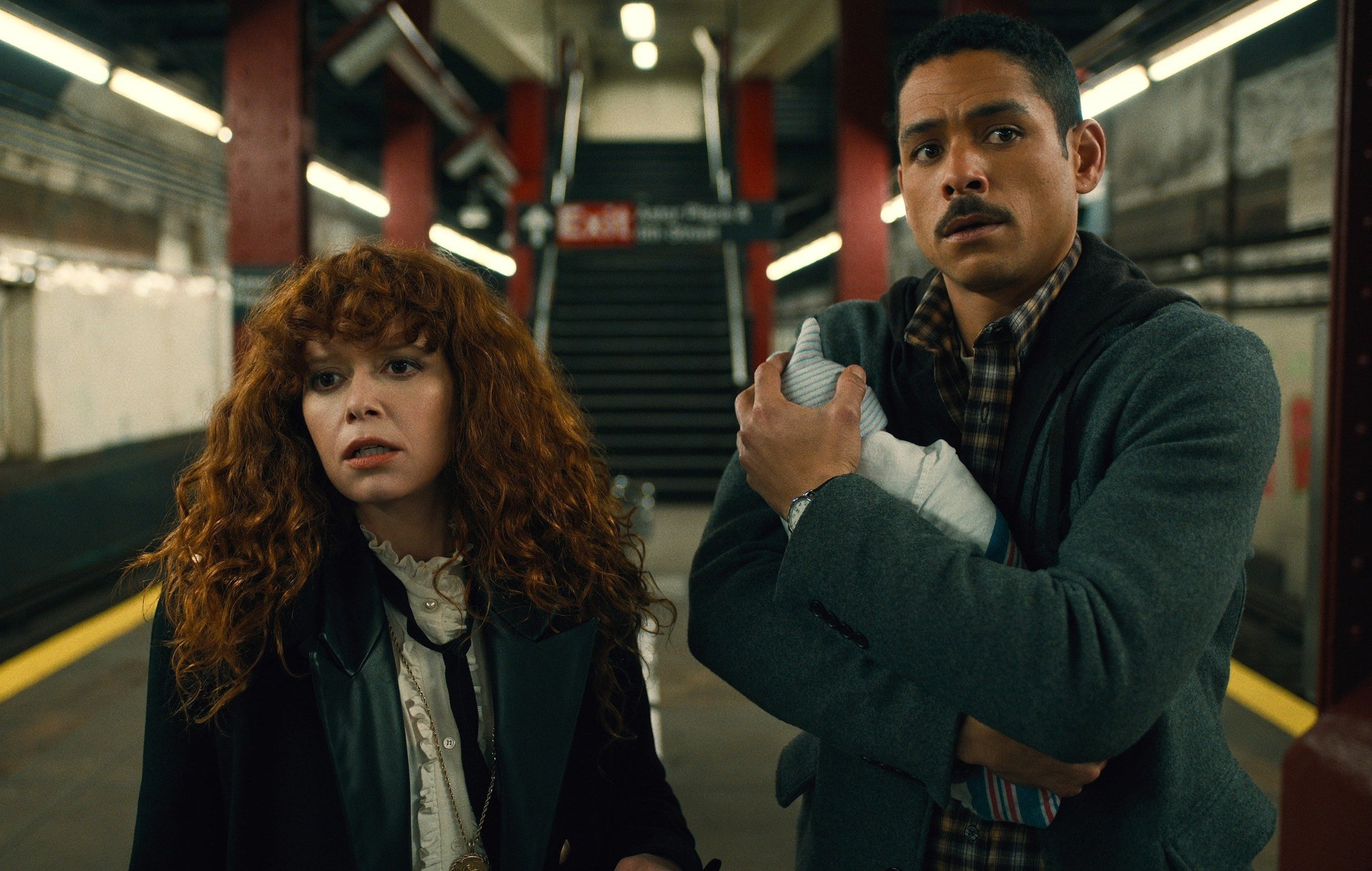 a woman and a man stand in a subway station with a baby looking concerned