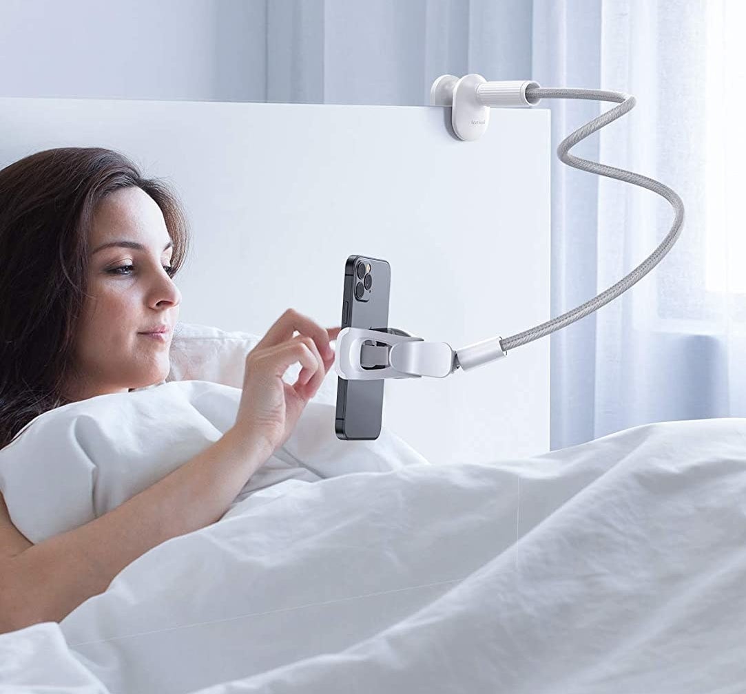 The flexible phone stand clipped onto a headboard while someone uses their phone