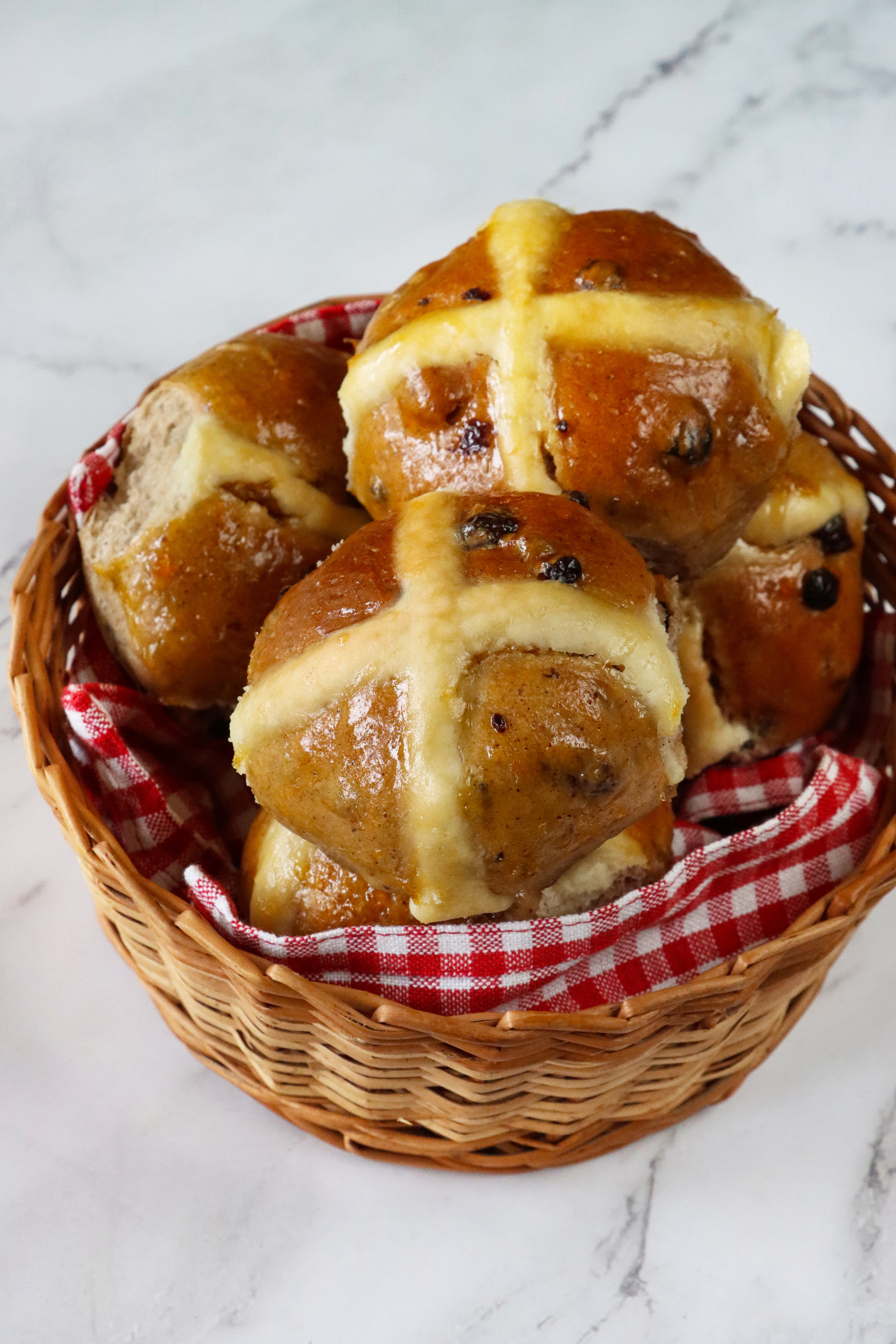 pile of freshly baked, homemade hot cross buns in a wicker basket lined with a red and white gingham cloth, home baking concept