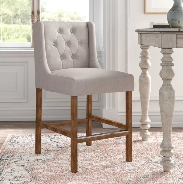 An image of a French beige bar and counter stool with a winged silhouette and distressed details