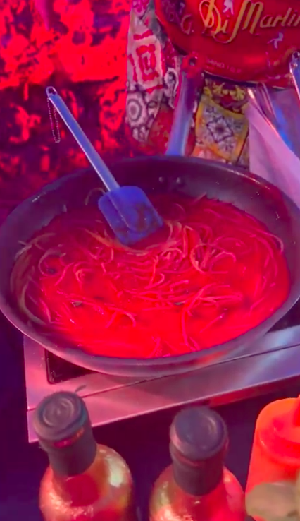 A large vat holds pasta covered in sauce